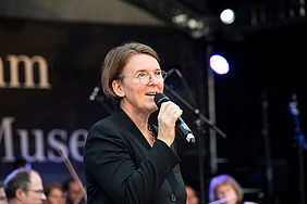 Steffi Bade-Bräuning auf der Bühne am Mikrofon kündigt das nächste Lied an.