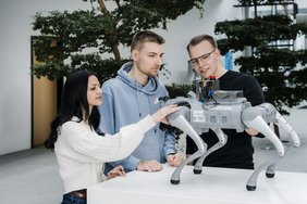 Eine Studentin und zwei Studenten mit einem Roboter Hund