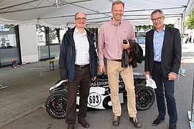 Three men stand in front of a car