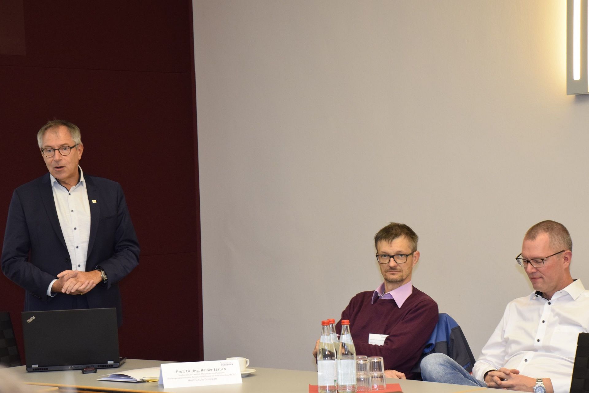 Ein Mann steht und spricht, zwei Männer hören zu