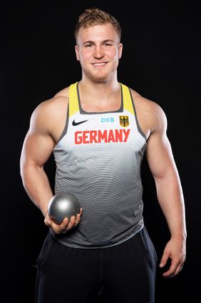 Ein junger Mann in grauß-weißem Trikot und einer Kugel in der rechten Hand.