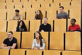 Männer und Frauen sitzen in einem Stufenhörsaal