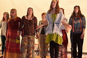 Solo-Sängerin in Hippie-Kleidung wird von Chor begleitet