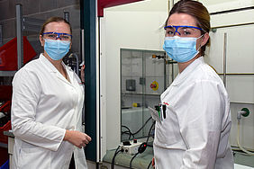 Zwei Studentinnen mit Laborkittel, Schutzbrille und Maske im Labor.