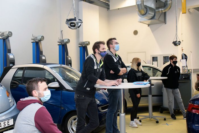 F&uuml;nf Studierende mit Maske in einer Fahrzeughalle.