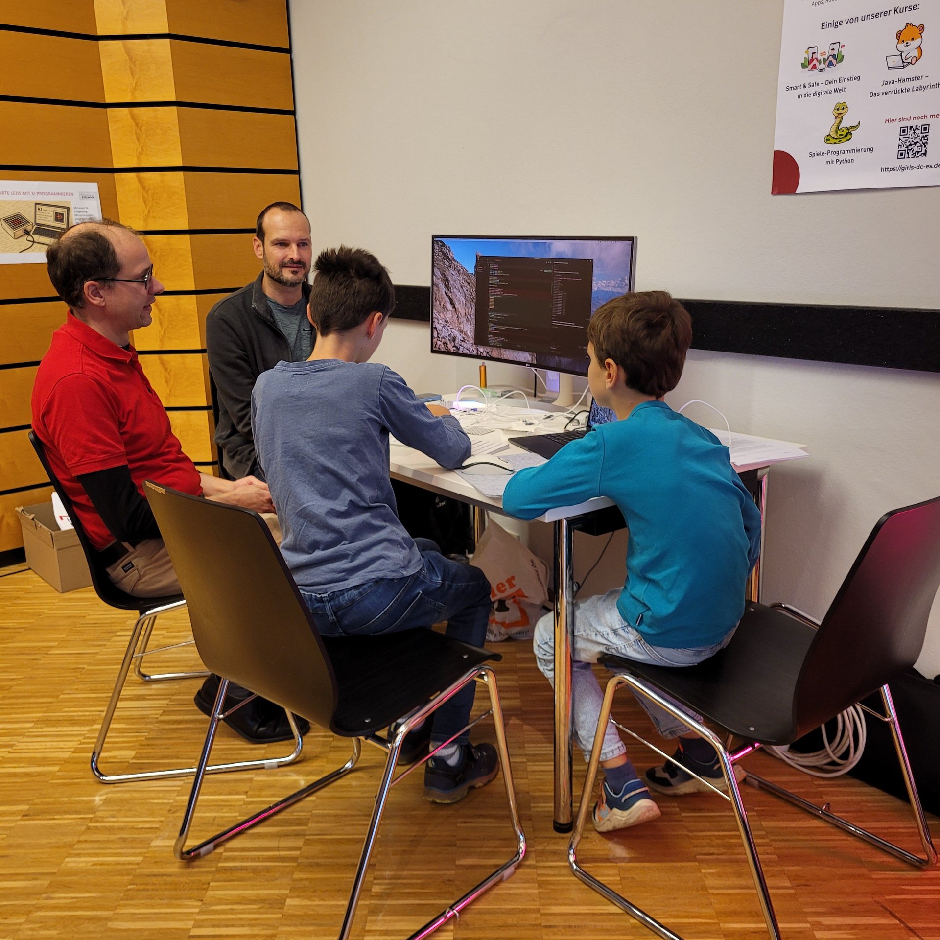 zwei Männer und zwei Jungen sitzen an einem Tisch vor einem PC