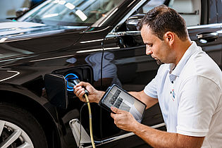 one person near a car checking the electronics of a hybrid vehicle