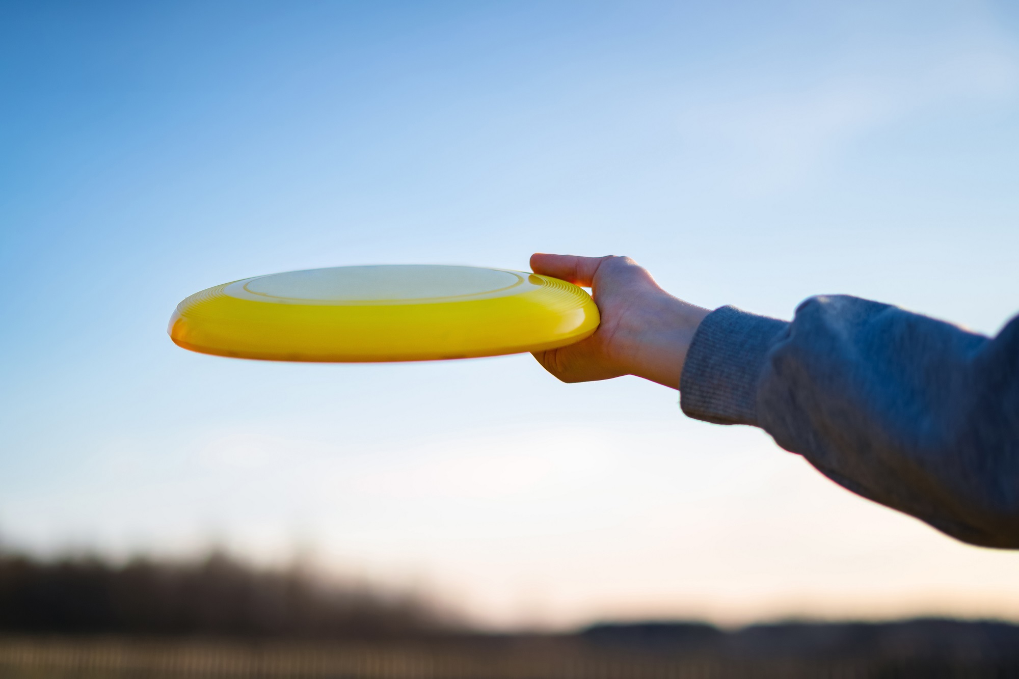 Hand holding yellow frisbee outside. Flaying frisbee outdoors with blue sky in the background Hand holding yellow frisbee outside. Flaying frisbee outdoors with blue sky in the background
