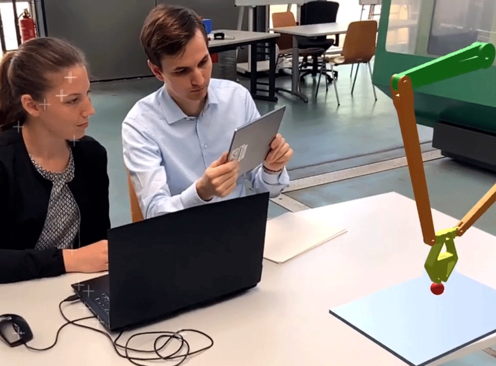 Eine junge Frau und ein junger Mann sitzen an einem Tisch, auf dem ein Laptop steht.