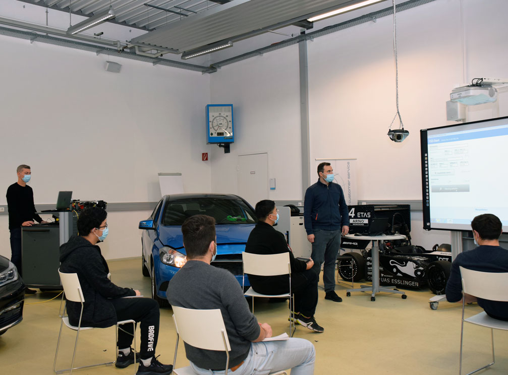 Fünf Studierende und zwei Lehrende in einer Fahrzeughalle.