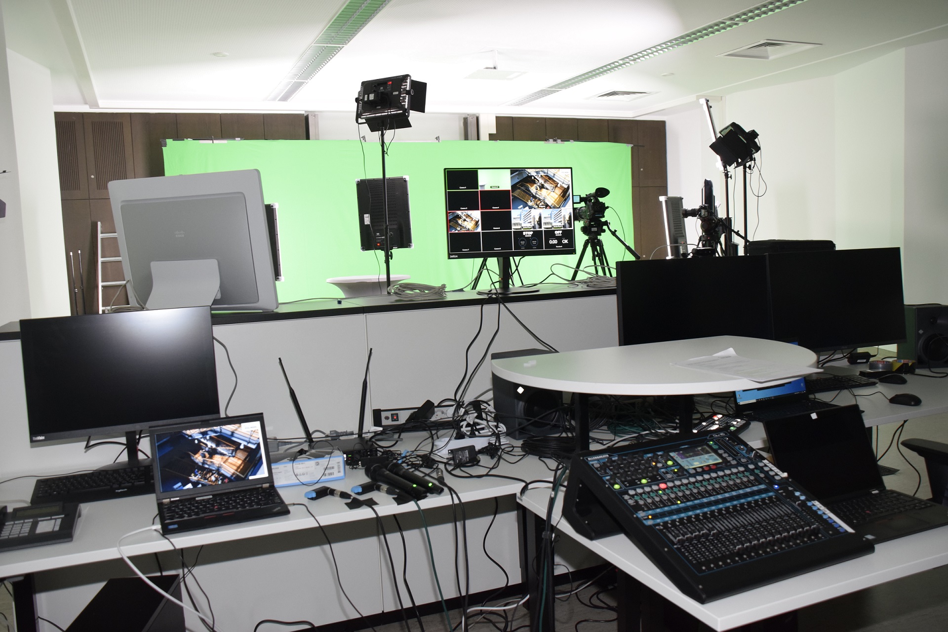 Es sind Mischpulte und Bildschirme zu sehen, im Hintergrund sind Kameras und ein Green Screen aufgebaut.