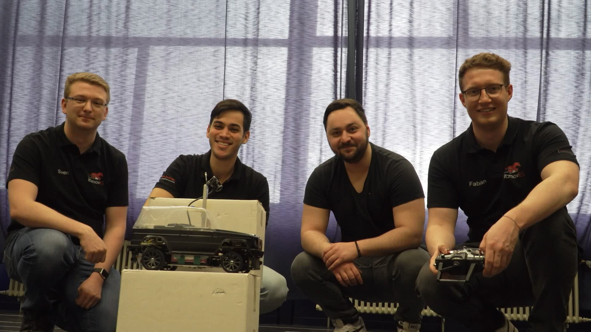 Gruppenfoto des it:movES Teams. Vier Studierende sitzen hinter ihren Modelfahrzeugen.