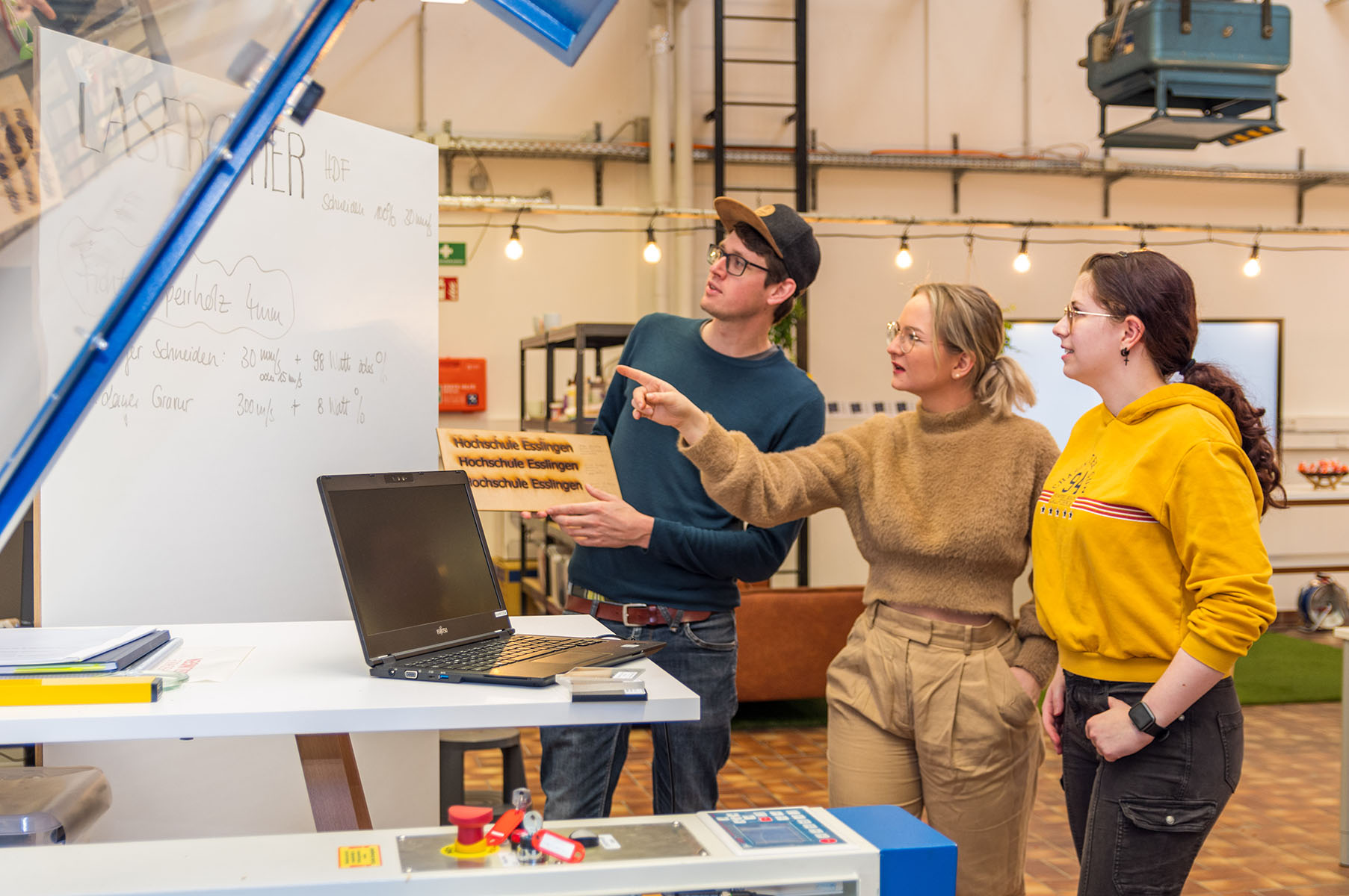 Zwei Frauen und ein Mann stehen im MakerSpacES! und unterhalten sich über den Lasercutter.