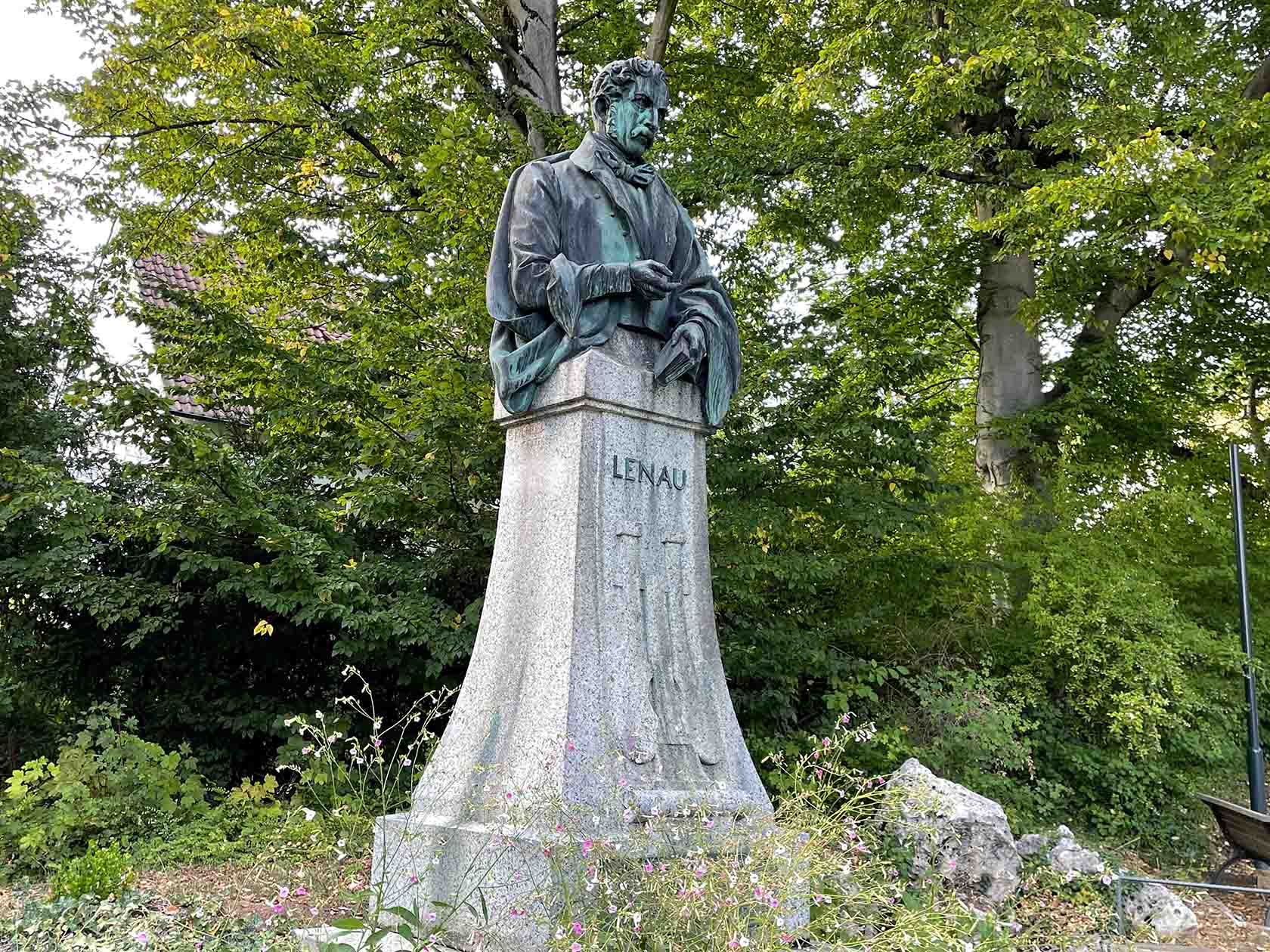 Auf einem Steinsockel in einem Park steht eine Bronzeskulptur von Lenau.