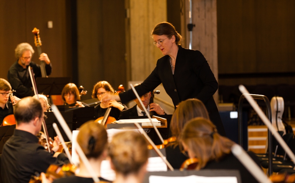 Steffi Bade-Bräuning, leiterin der Hochschulmusik dirigiert die Musikerinnen und Musiker bei einem Lied.