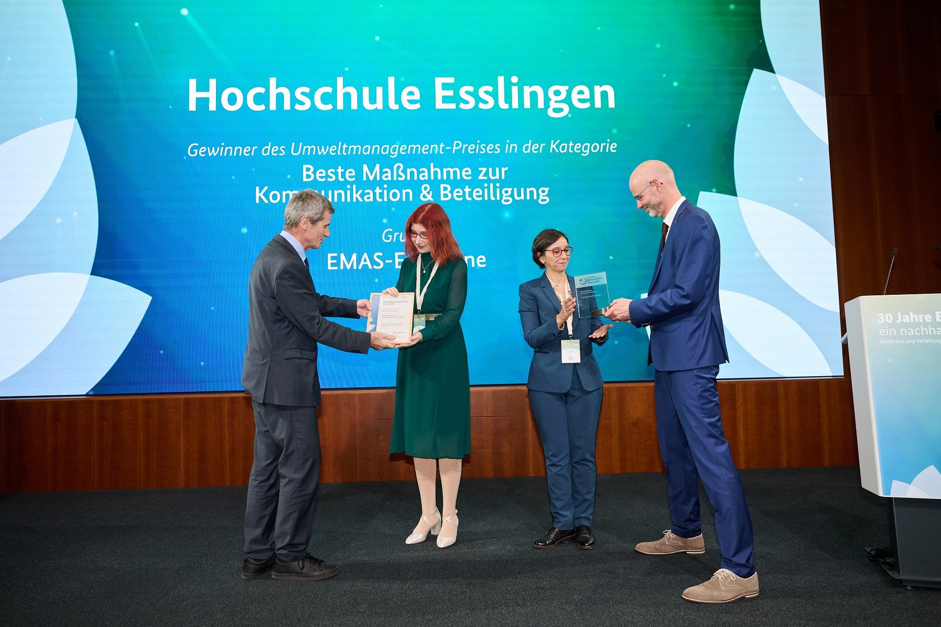 Zwei Männer übergeben zwei Frauen eine Urkunde und einen Preis