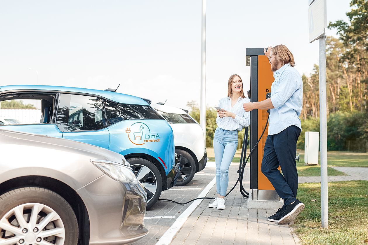 Young adult friends talking and charging electric car